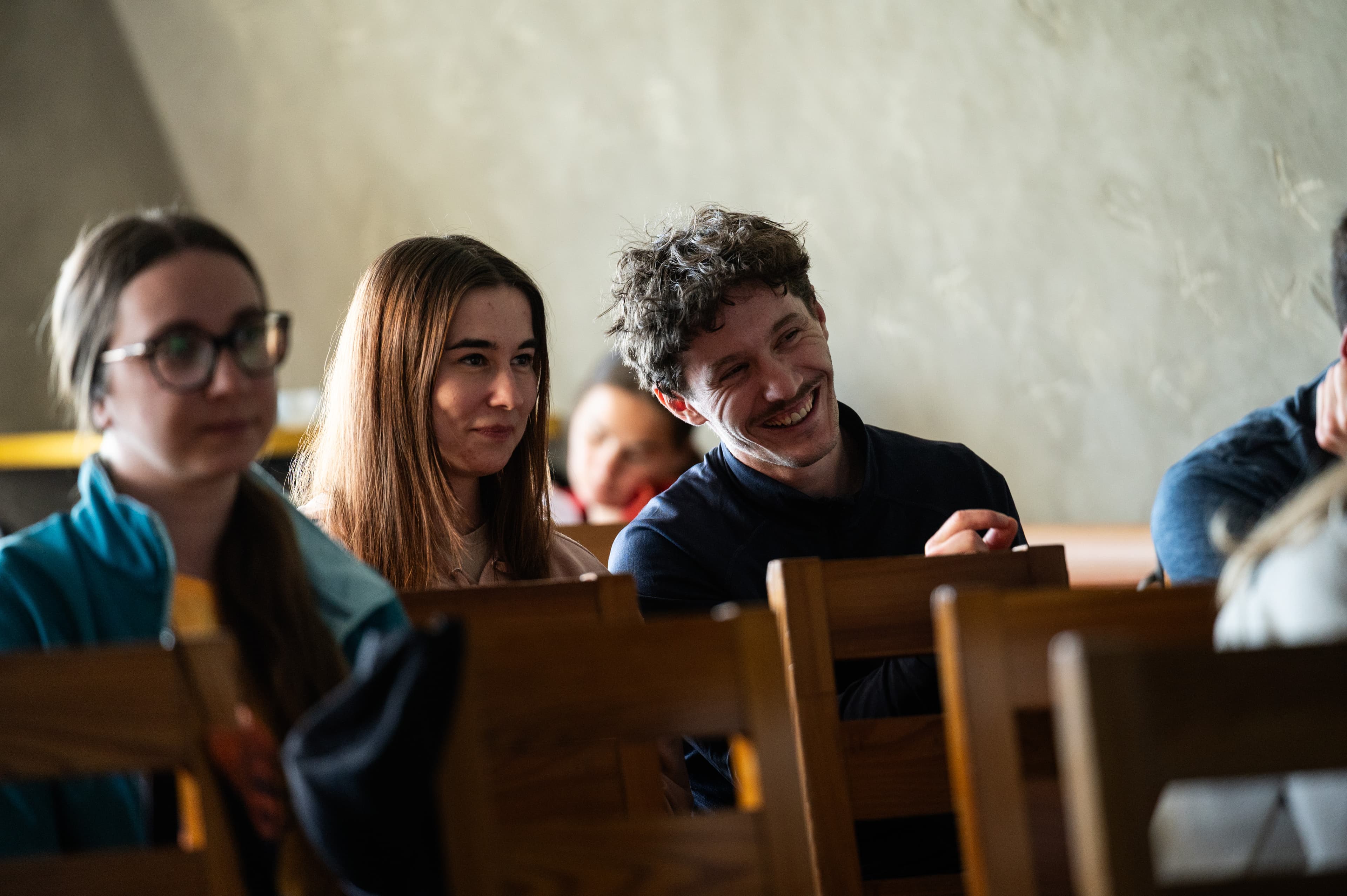 Účastníci sedia v lavici a sledujú program.